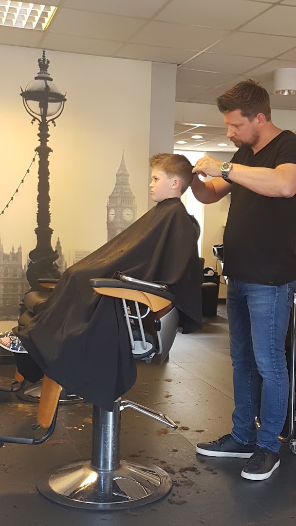 Kapper knipt een jongetje bij Max Haarmode, met de Londen-muurschildering op de achtergrond